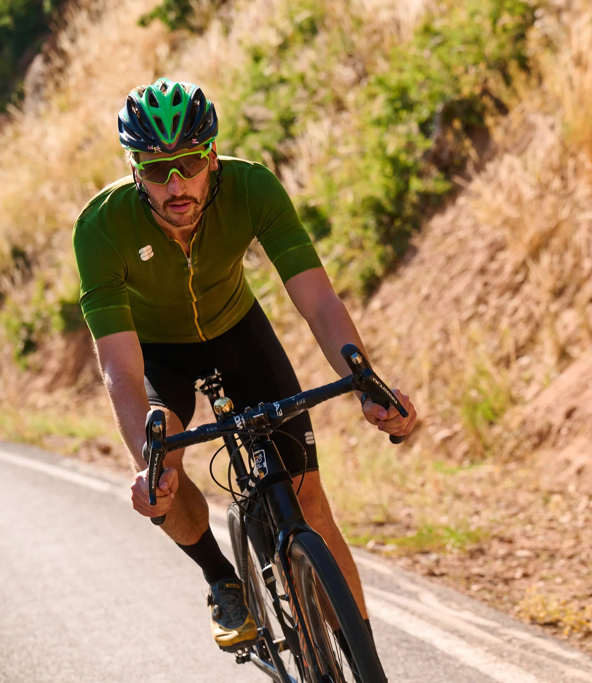 Cyclist in green jersey and helmet riding on a road with natural scenery.