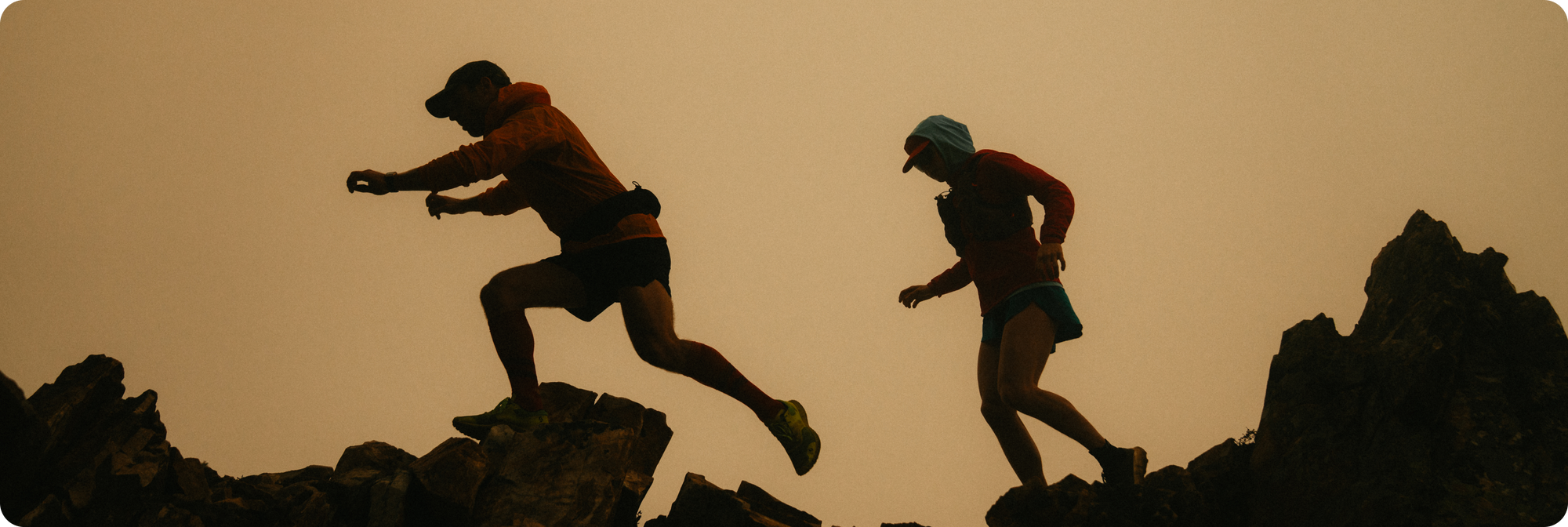 Silhouettes of two people running on rocky terrain against a sunset sky.