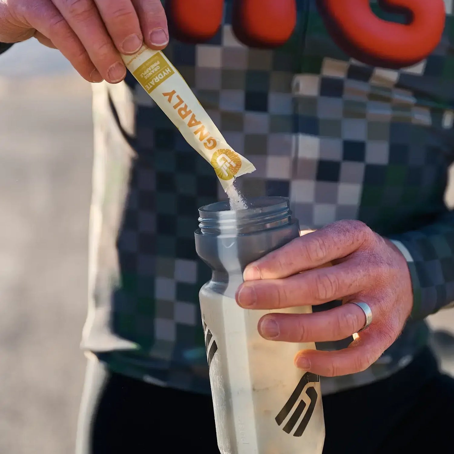 Cyclist pouring a Gnarly Hydrate stick into a water bottle